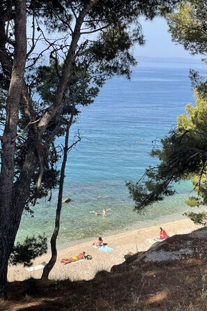 A beach with clear water, people swimming, and sunbathers on the sand.