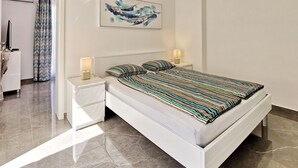 Un dormitorio moderno con cama blanca, ropa de cama a rayas, dos lámparas de noche, una obra de arte en la pared y una lámpara de techo.