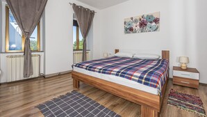 Un dormitorio con una cama de madera, una mesita de noche, una lámpara, un radiador y una ventana con cortinas.