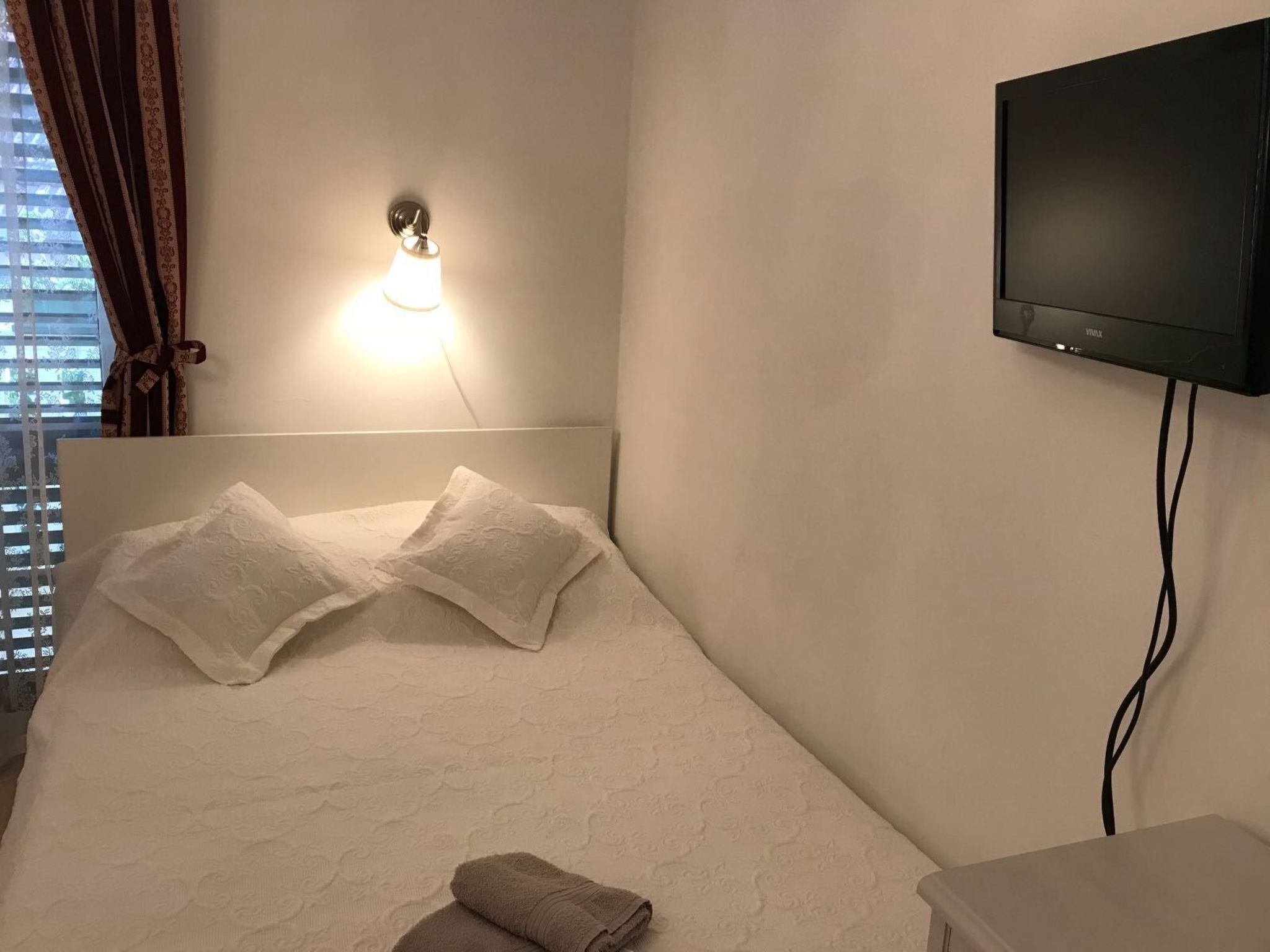 A hotel room with a bed, a wall-mounted TV, and a window with curtains.