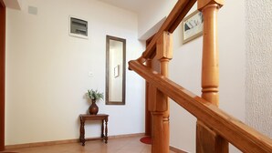 Una escalera de madera con barandilla, una mesita con un florero y un espejo en la pared.