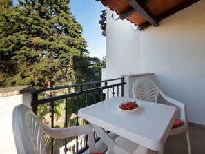 A balcony with a white table and chairs, a basket of cherries, and a view of trees. - Svoboda 4 by Interhome (Krk/Šilo)