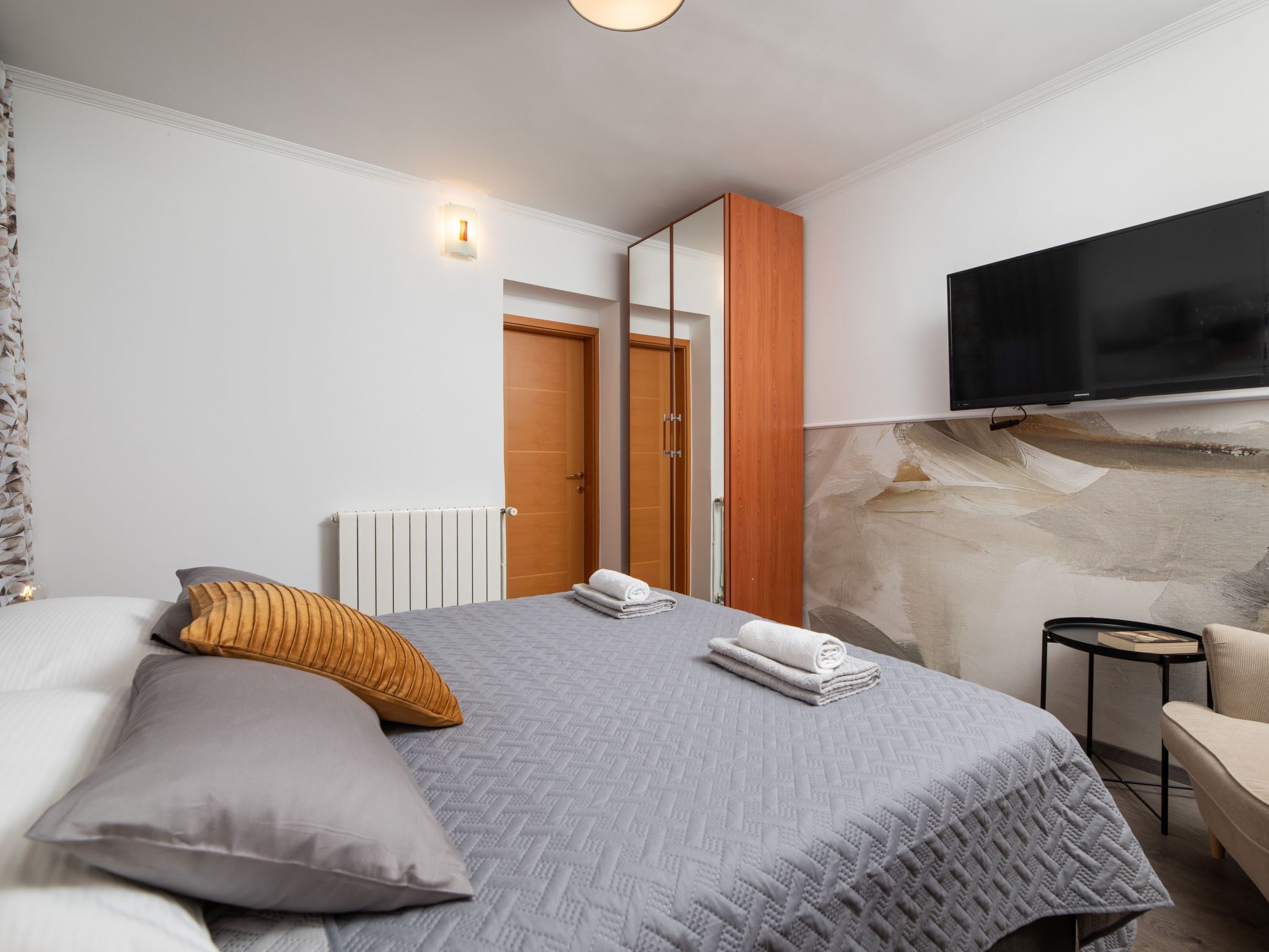 A bedroom with a bed, pillows, a TV, a wardrobe, and a small table.