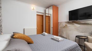 A bedroom with a bed, pillows, a TV, a wardrobe, and a small table.