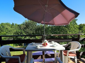 Eine Terrasse mit Tisch für zwei Personen, einem großen Sonnenschirm und Blick auf ein bewaldetes Gebiet.