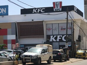 A KFC restaurant with a large sign, parked cars, and a delivery truck in front. - Charming Urban Teranga: An apartment in a great location. Near the Corniche, downtown (Dakar)