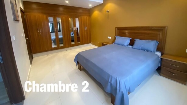 A bedroom with a large bed, wooden wardrobe, and a nightstand. - Sweet Urban Teranga: Very well located apartment. Near the corniche, the center (Dakar)