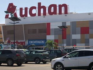 Ein Einkaufszentrum mit einer großen 'uchan'-Werbetafel, einem 'Decathlon'-Geschäft und mehreren parkenden Autos.