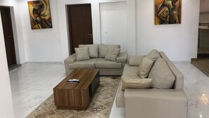 A modern living room with a beige sectional sofa, a wooden coffee table, and abstract paintings on the walls. - Sweet Urban Teranga: Very well located apartment. Near the corniche, the center (Dakar)