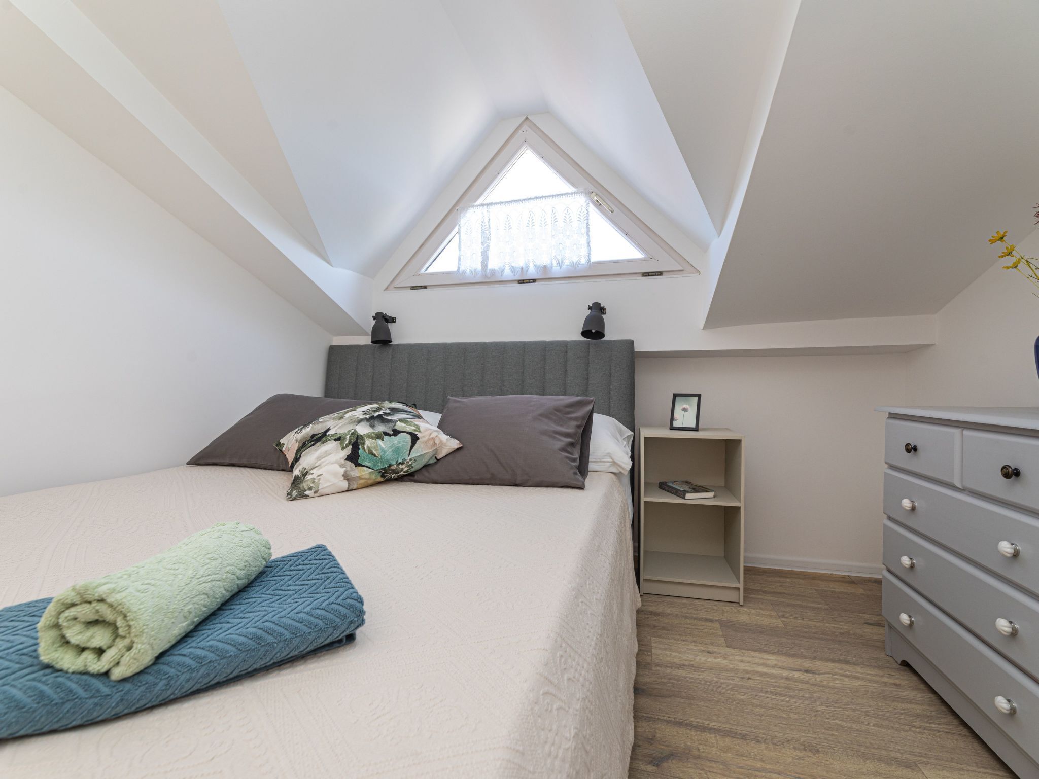 Una camera da letto con soffitto spiovente, un letto con cuscino, un comodino con lampada e una cassettiera.
