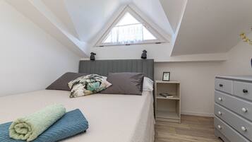 Una camera da letto con soffitto spiovente, un letto con cuscino, un comodino con lampada e una cassettiera.