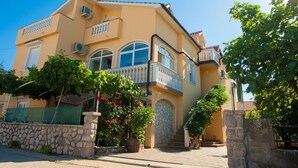 A two-story house with a stone facade, a balcony with white balustrades, and a large arched window. - Gemütliche Ferienwohnung Tina 4 by Interhome (Krk/Šilo)