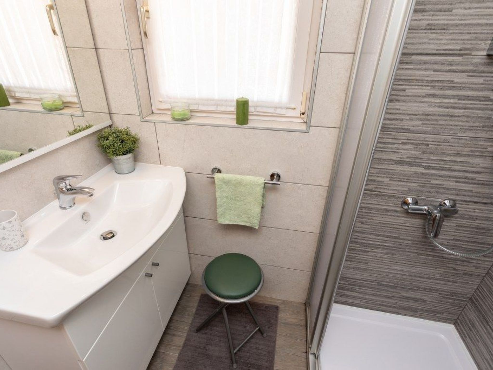 A bathroom with a white sink, green stool, and a shower area.