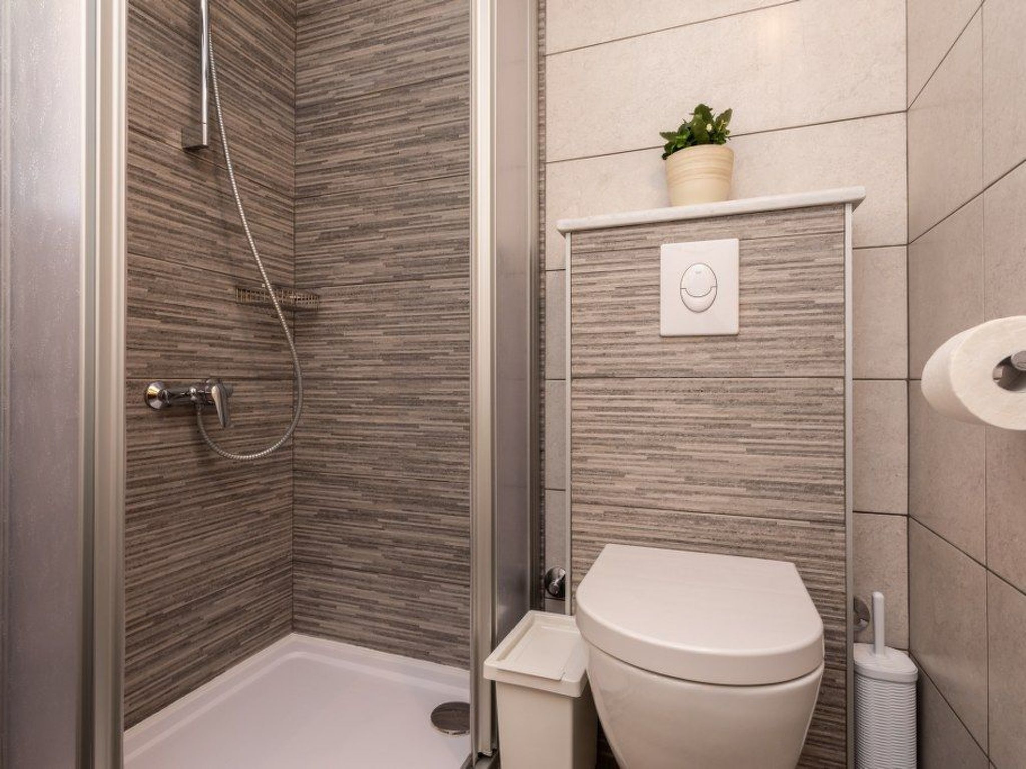 Et moderne badeværelse med bruser, toilet og en lille plante på væggen.