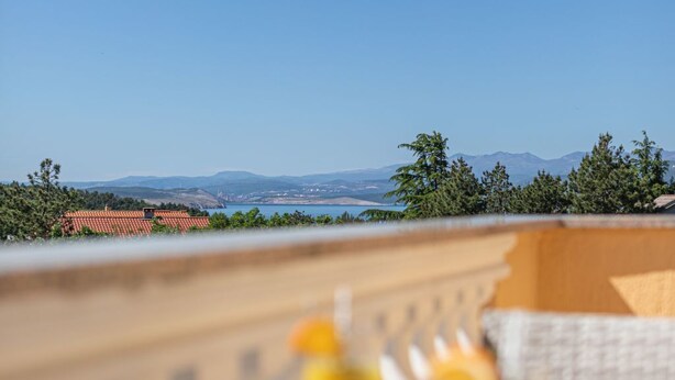 A dining table with a plate of food and drinks, overlooking a scenic view of a coastline and distant hills. - Gemütliche Ferienwohnung Tina 4 by Interhome (Krk/Šilo)