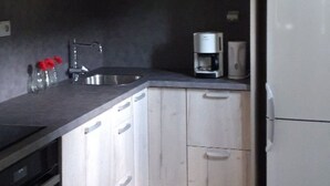 Une cuisine avec des meubles de rangement en bois, un plan de travail noir, un évier en acier inoxydable, une machine à café et un réfrigérateur blanc.