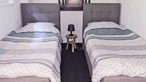 Une chambre avec deux lits, une petite table avec une lampe et un tableau au mur.