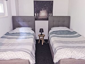Une chambre avec deux lits, une petite table avec une lampe et un tableau au mur.