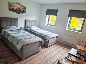 A bedroom with two beds, a window with a view of trees, and a small table with a chair.