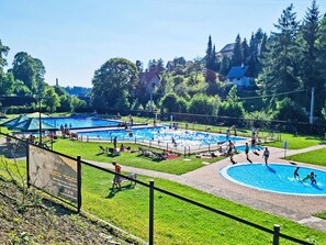 A swimming pool area with multiple pools, surrounded by grass and trees.