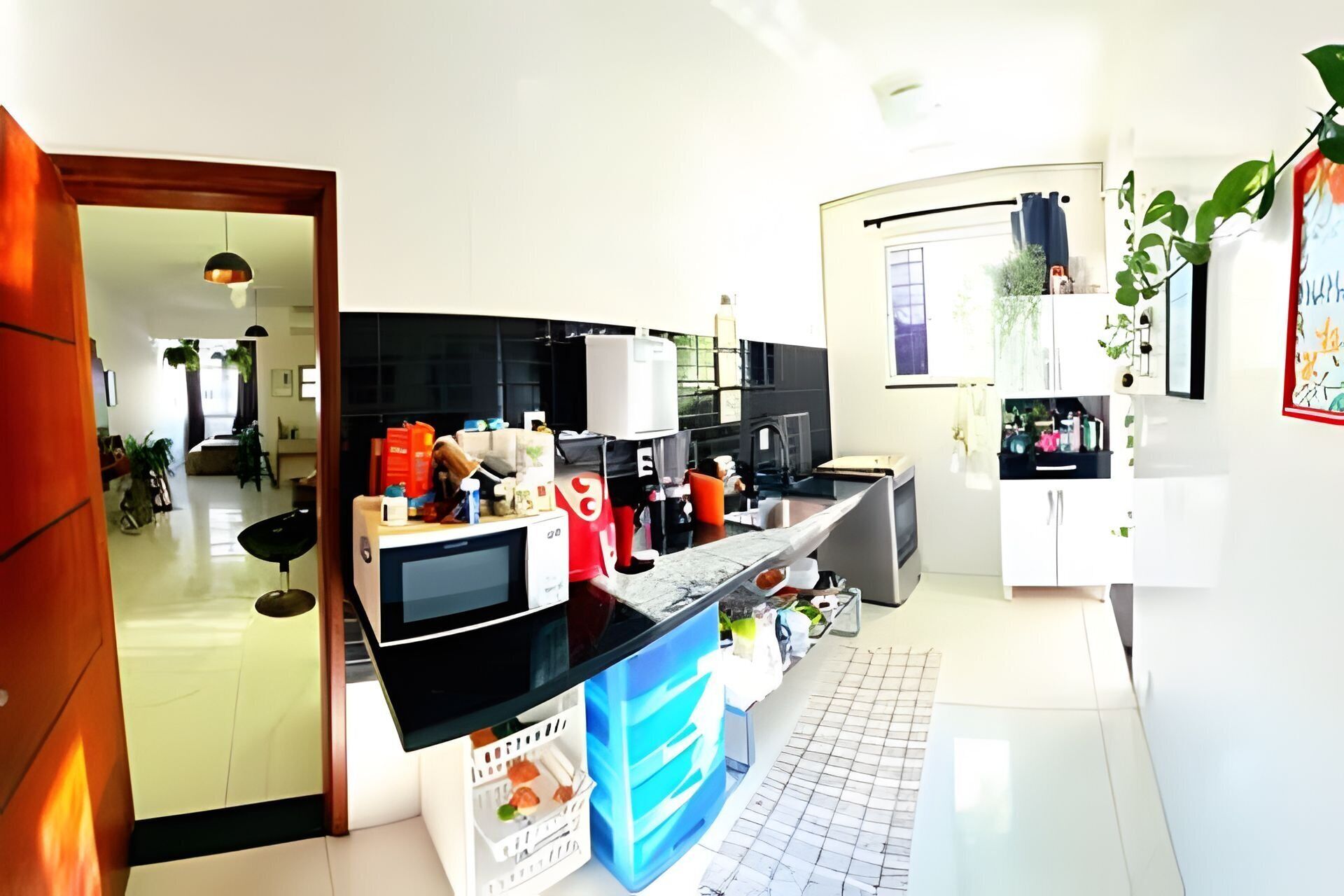 Eine moderne Küche mit schwarzem Arbeitsplatz, weißen Schränken und einer gefliesten Spritzschutzwand. Es gibt eine Mikrowelle, eine Kaffeemaschine und ein Spülbecken. Das helle Ambiente wird durch natürliches Licht von einem Fenster erzeugt.