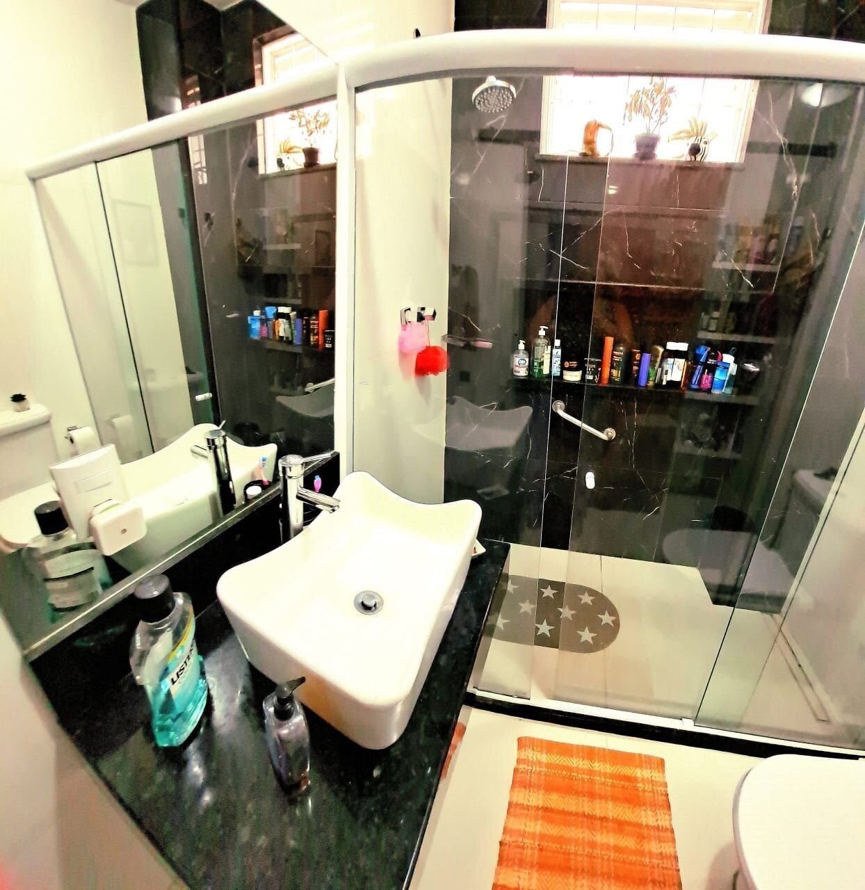 Un baño moderno con lavamanos blanco, cabina de ducha con cristal y un espejo grande.