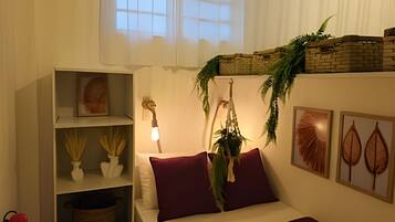 Un dormitorio con cama, una mesita de noche, una estantería con objetos decorativos, una planta colgante y cuadros en la pared.