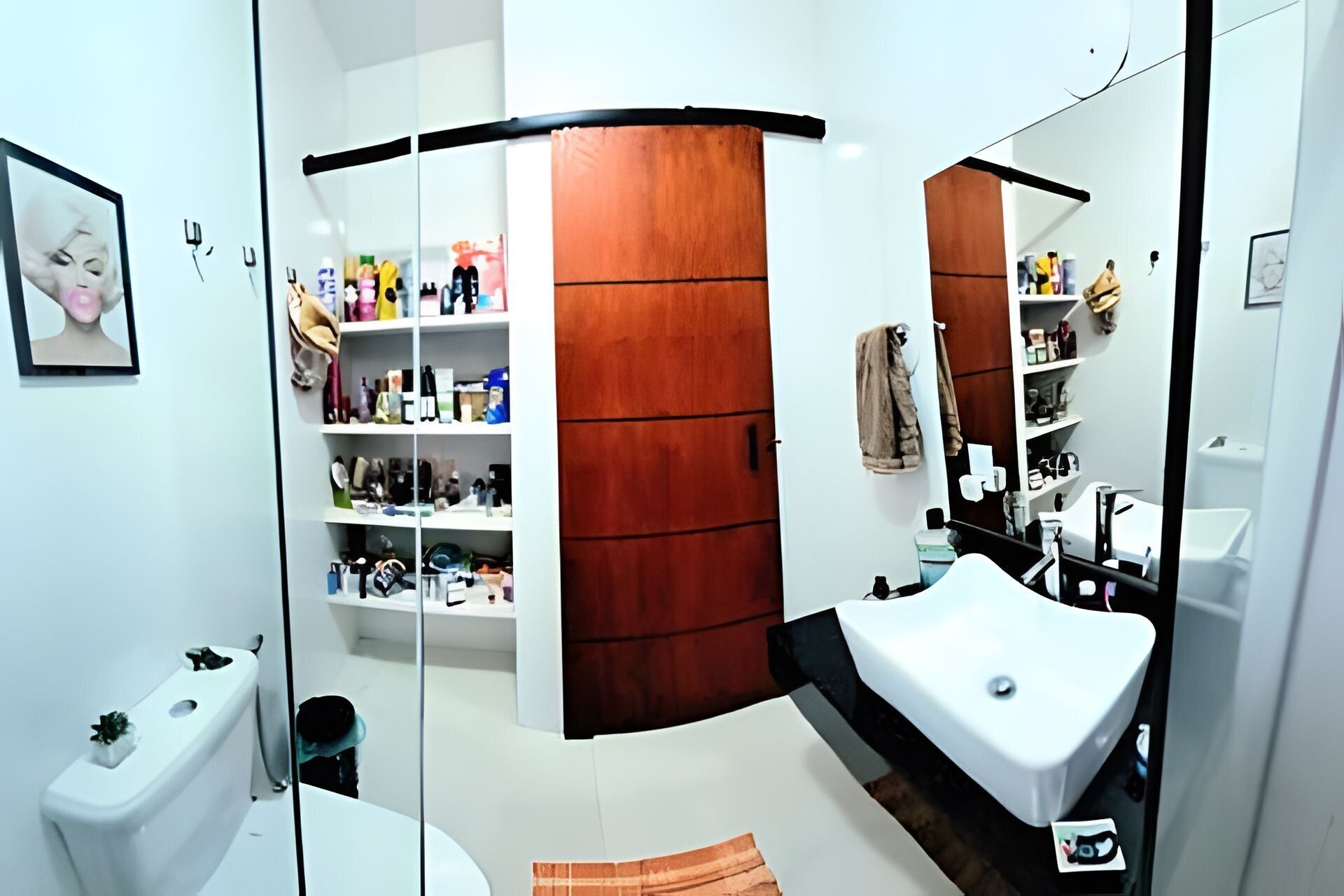 A modern bathroom with a white sink, wooden vanity, and shelves with toiletries.