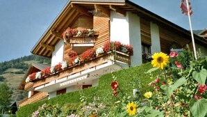 Ein traditionelles Chalet mit hölzernen Balkonen, die mit Blumen geschmückt sind, vor einer Bergkulisse.