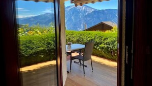 Eine Terrasse mit Tisch und Stühlen, Blick auf die Berge und ein Holzhäuschen im Hintergrund.