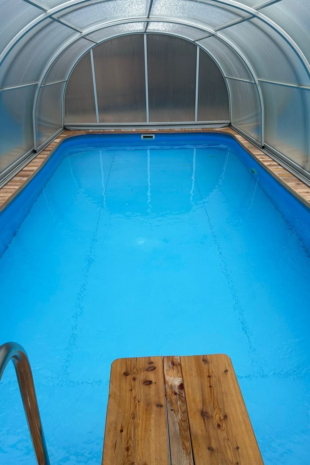 An indoor swimming pool with a wooden deck and a metal ladder.