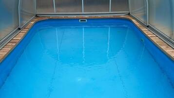 An indoor swimming pool with a wooden deck and a metal ladder.