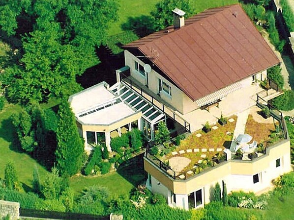 Une maison moderne à deux étages, dotée d’un toit plat, d’un patio couvert et d’une petite terrasse.