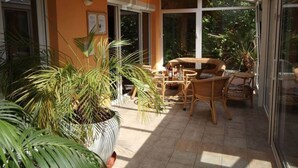 A sunlit patio with wicker furniture, large windows, and potted plants. - Pool-Wellness JOSKA by Interhome (Mladá Boleslav)