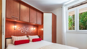 A bedroom with a bed, wooden cabinets, a wall-mounted light fixture, and a window with a view of greenery. - Ivona mit Terrasse und Außendusche by Interhome (Dubrovnik)