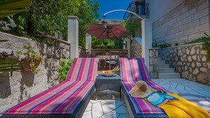 A sunlit outdoor seating area with two striped lounge chairs, a small table, and a decorative umbrella. - Ivona mit Terrasse und Außendusche by Interhome (Dubrovnik)