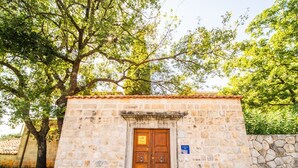 Un edificio in pietra con una porta di legno, un cartello sopra la porta e una targa blu a destra.