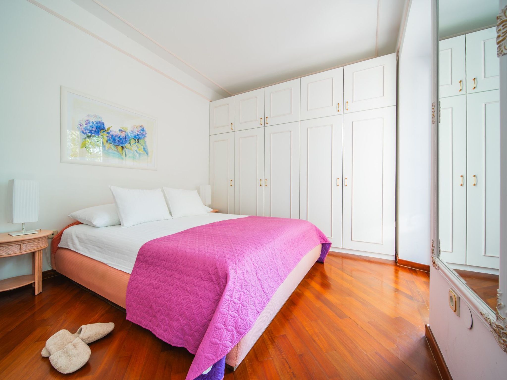 Une chambre à coucher avec un lit, une armoire blanche, un plancher en bois et un tableau au mur.