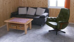 A living room with a sofa, a green leather armchair, a small wooden coffee table, and a painting on the wall. - Ferien im grünen rechts by Interhome (Haldi b. Schattdorf)