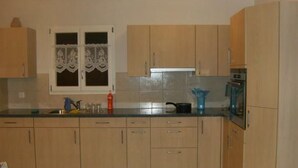 A kitchen with light wooden cabinets, a window with lace curtains, and a stove. - Ferien im grünen rechts by Interhome (Haldi b. Schattdorf)
