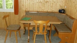 A dining area with a wooden table and bench seating, a window with curtains, and a patterned wall. - Ferien im grünen rechts by Interhome (Haldi b. Schattdorf)