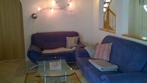 Olohuoneessa on violetti sohva, lasinen sohvapöytä ja seinälle ripustettu valonauha.