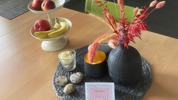 Uma mesa de jantar com um suporte escalonado para frutas, um vaso com flores, uma vela e um pequeno cartão.