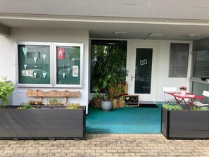 Une entrée moderne, agrémentée d’un banc en bois, de plantes en pot et d’une petite table avec des chaises.