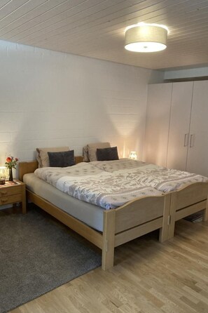 Een slaapkamer met een houten bed, een nachtkastje met een lamp en een kledingkast.
