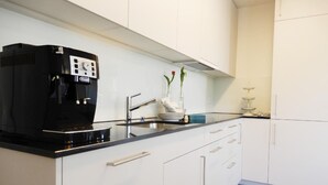 Uma cozinha moderna com armários brancos, uma máquina de café preta, uma pia de aço inoxidável e um vaso com flores na bancada.