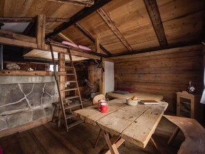 A rustic wooden cabin interior with a stone fireplace, a wooden table with a red mug, a bunk bed, and a ladder. - Kirschbaumhütte by Interhome (Gündlischwand)