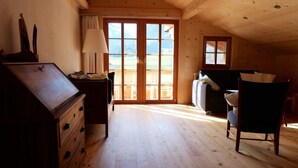 Un intérieur en bois avec un bureau, une chaise et une vue dégagée sur l’extérieur grâce à une grande porte-fenêtre coulissante.