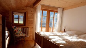Une chambre dans une cabane en bois, avec un lit, une chaise, un radiateur et une fenêtre avec des rideaux.