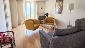 Un salon comprenant deux fauteuils, un canapé, une table basse, un téléviseur et un radiateur.